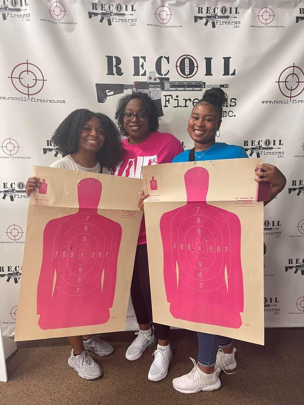 Three friends showing off their targets in front of the Recoil Firearms backdrop