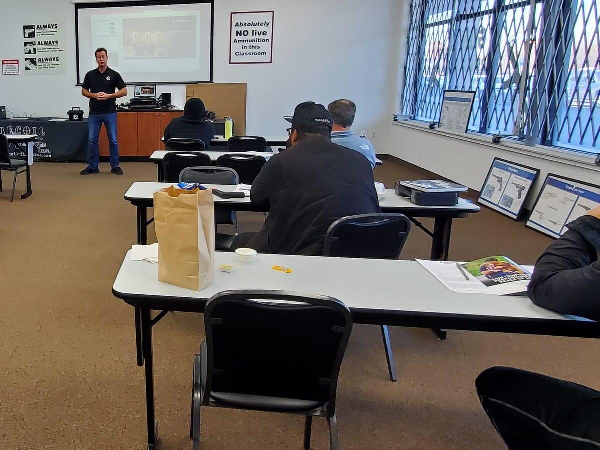 An instructor teaching a concealed pistol class, seen from the back of the classroom